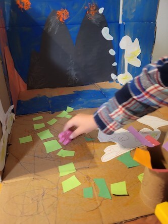 Child playing with toy dinosaur in dinosaur habitat craft